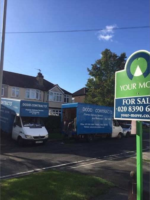 Dodd Removals vans working at a property with a For Sale board outside
